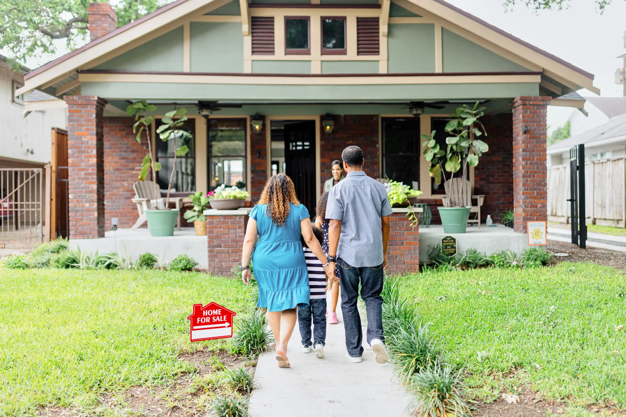 Family walking toward house with for-sale sign